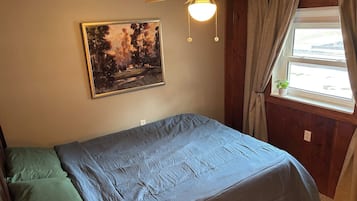Ett sovrum med en säng, en takfläkt, ett fönster med gardiner och en tavla på väggen.