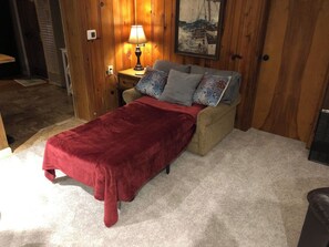Ein Zimmer mit einem Bett, einem Nachttisch, einer Lampe und einem Bild an der Wand.