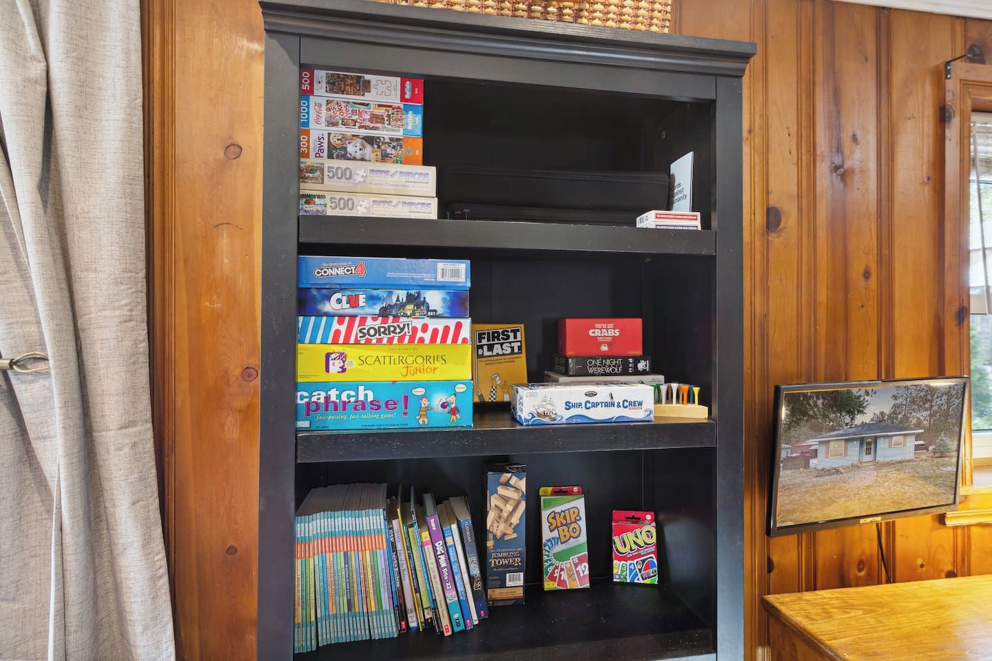 A bookshelf with various board games and a framed picture on a wooden wall.