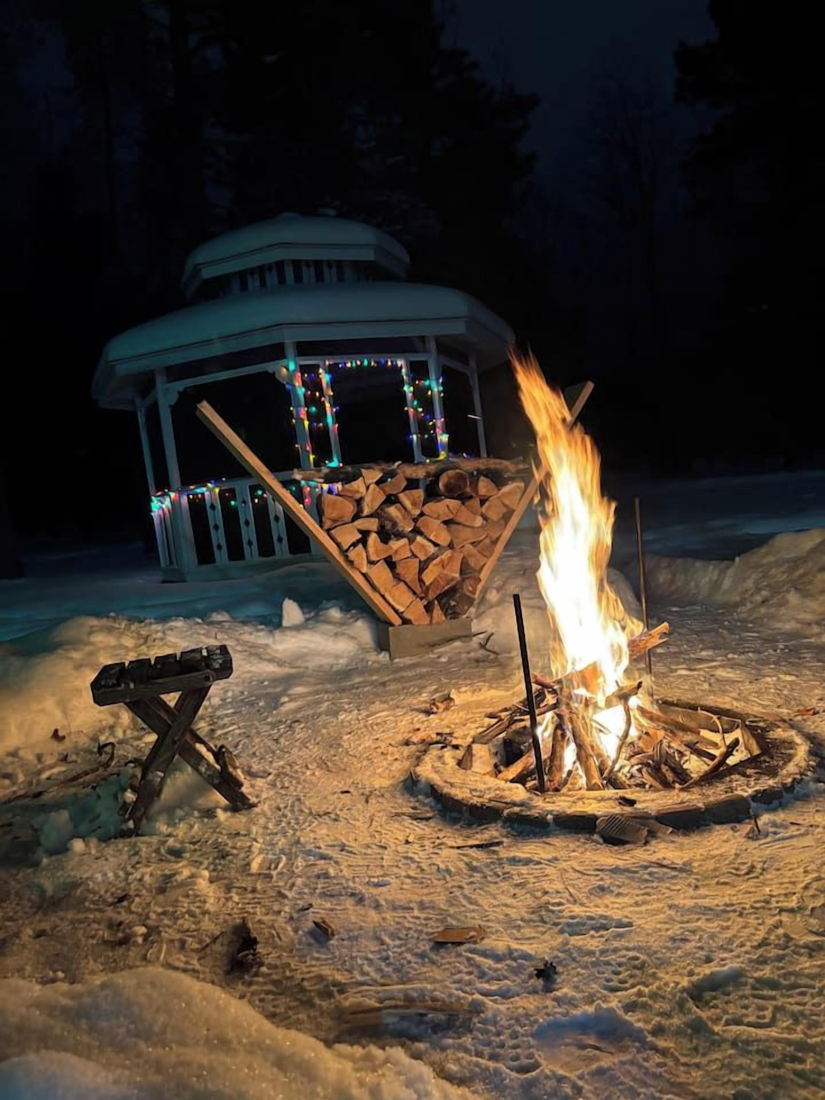 A snow-covered outdoor area with a fire pit and a gazebo adorned with lights.
