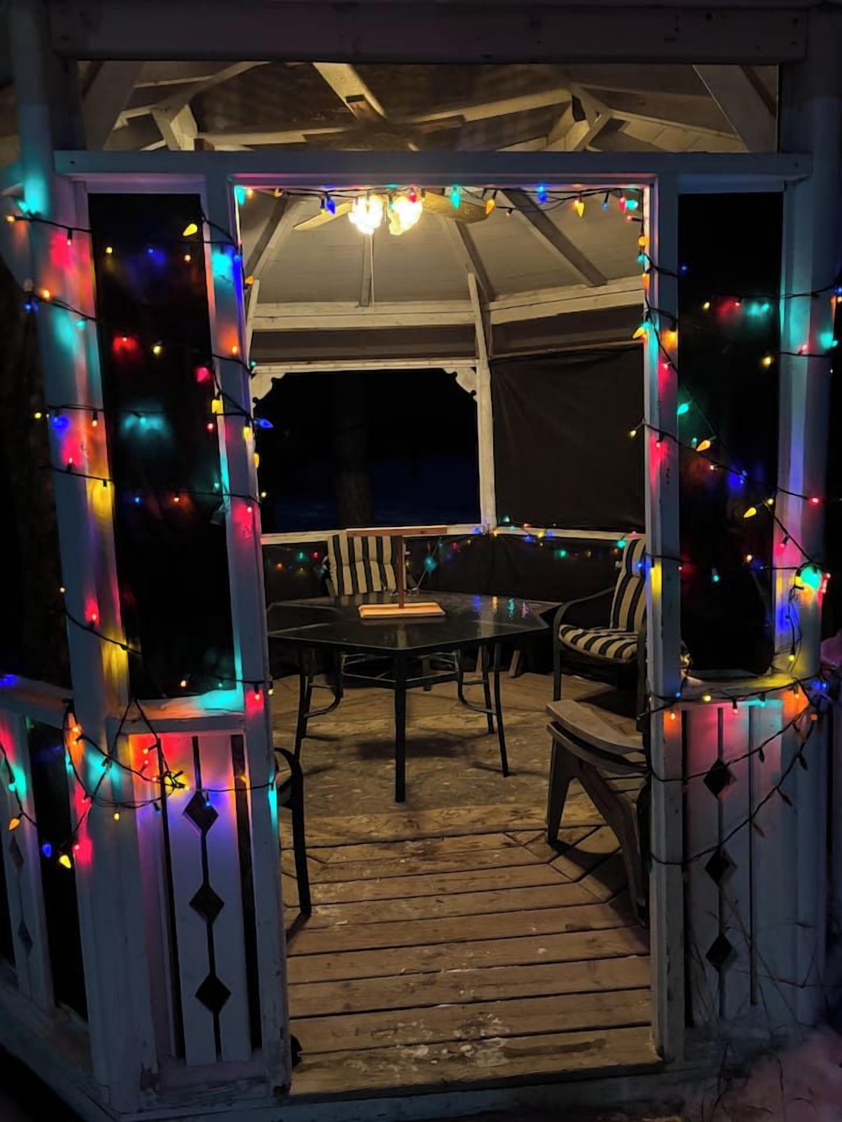 An outdoor patio area with a table and chairs, surrounded by a white structure with decorative string lights.