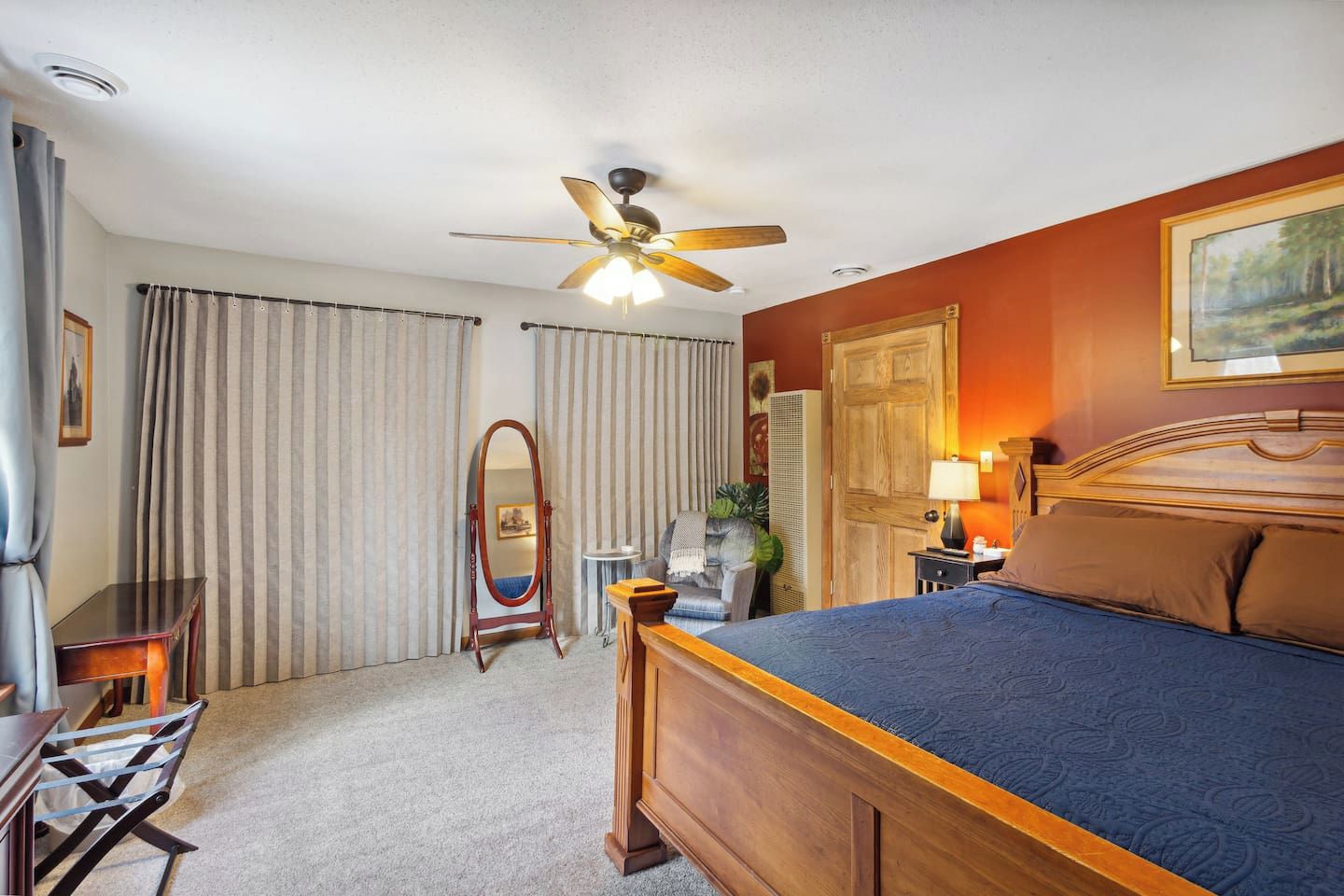 A hotel room with a bed, a desk, a chair, a ceiling fan, and a large mirror.