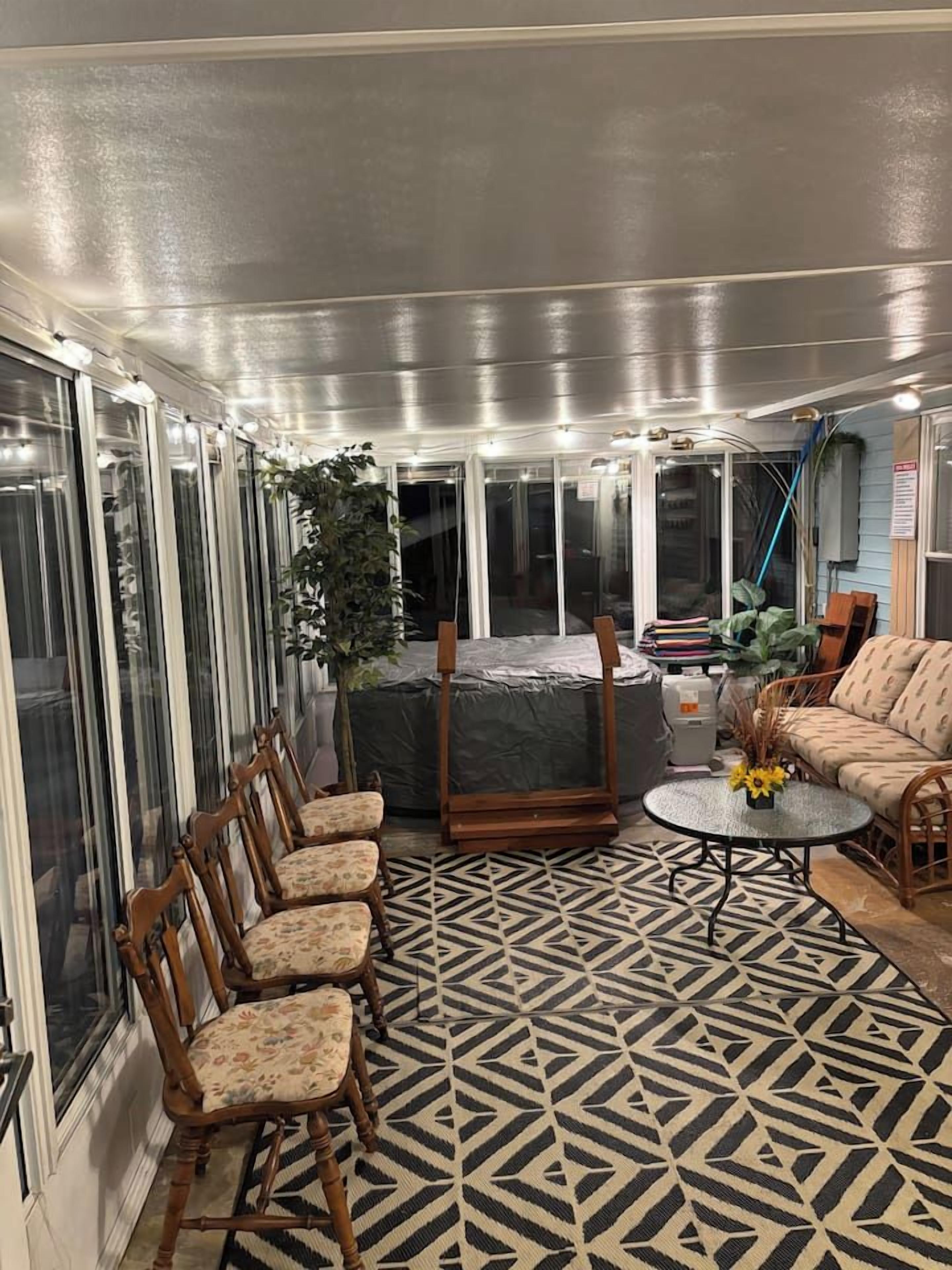 A covered patio area with a patterned floor, a seating arrangement, and a potted plant.