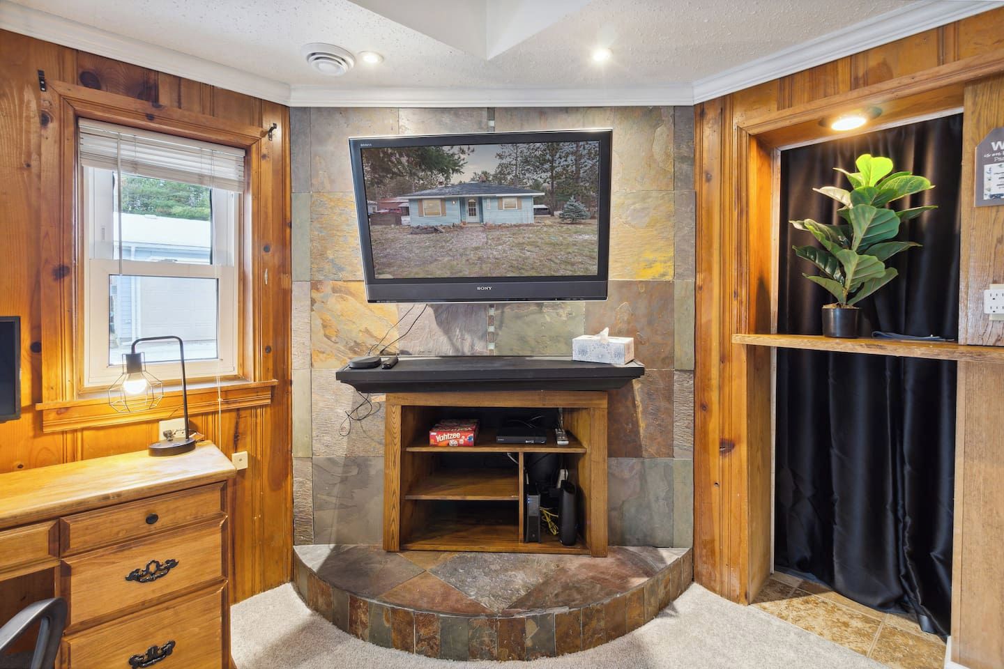 Une pièce avec un bureau en bois, un téléviseur fixé au mur et un mur décoratif en pierre.