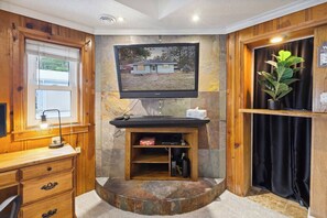 A room with a wooden desk, a mounted television, and a stone accent wall.