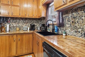 Una cocina con armarios de madera, protector contra salpicaduras de piedra, un lavamanos negro y varios electrodomésticos.