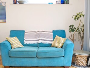 Un canapé de couleur turquoise agrémenté de coussins à rayures et à motifs, une petite table d’appoint avec un plateau en verre et une plante en pot.