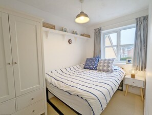 Une chambre à coucher comprenant un lit, une table de chevet, une armoire, une fenêtre avec des rideaux et un luminaire suspendu.
