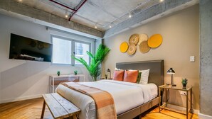 Un dormitorio moderno con una cama grande, un banco de madera, un escritorio y una planta en maceta.