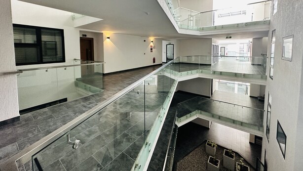 A multi-level interior with glass railings, tiled floors, and a central open space. - Cozy 2 bedroom apartment in Labone (Accra)