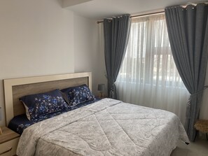 Une chambre à coucher avec un lit, une table de chevet, une lampe et une fenêtre avec des rideaux.