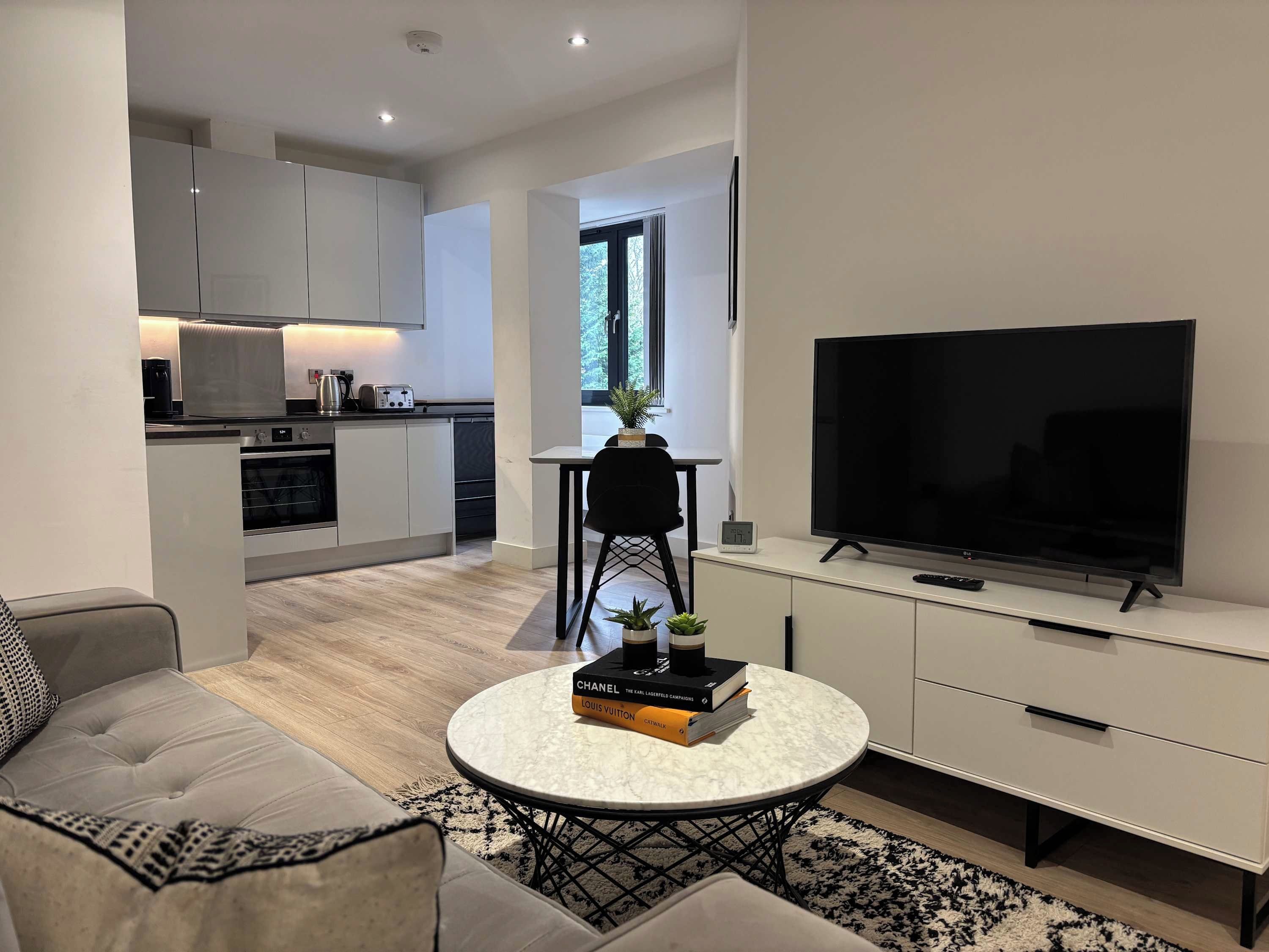 Un soggiorno moderno con un divano, un tavolino da caffè con libri, una TV e una cucina sullo sfondo.