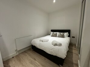 Een slaapkamer met een zwart hoofdeinde, wit beddengoed en twee kussens.