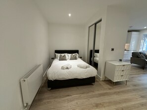 Une chambre moderne avec un grand lit, une table de chevet, un miroir et une vue sur le salon.