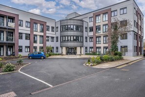 A modern multi-story building with a central entrance, parking area, and a blue car parked in front. - Solihull Studio • WiFi • NEC • BHX (Solihull)