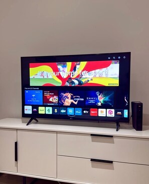 A flat-screen TV on a white cabinet with a digital interface displaying various channels and a sports event. - Solihull Studio • WiFi • NEC • BHX (Solihull)