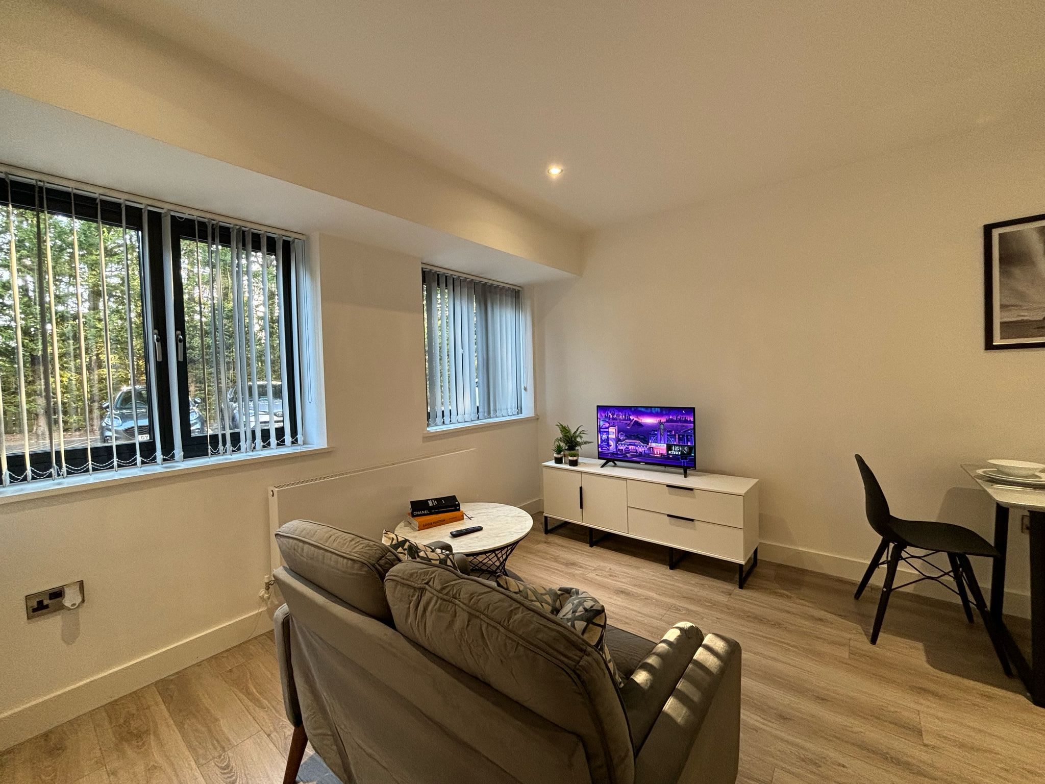 Una sala moderna con un sofá, una mesa de centro, un televisor y un comedor con una silla y una mesita.