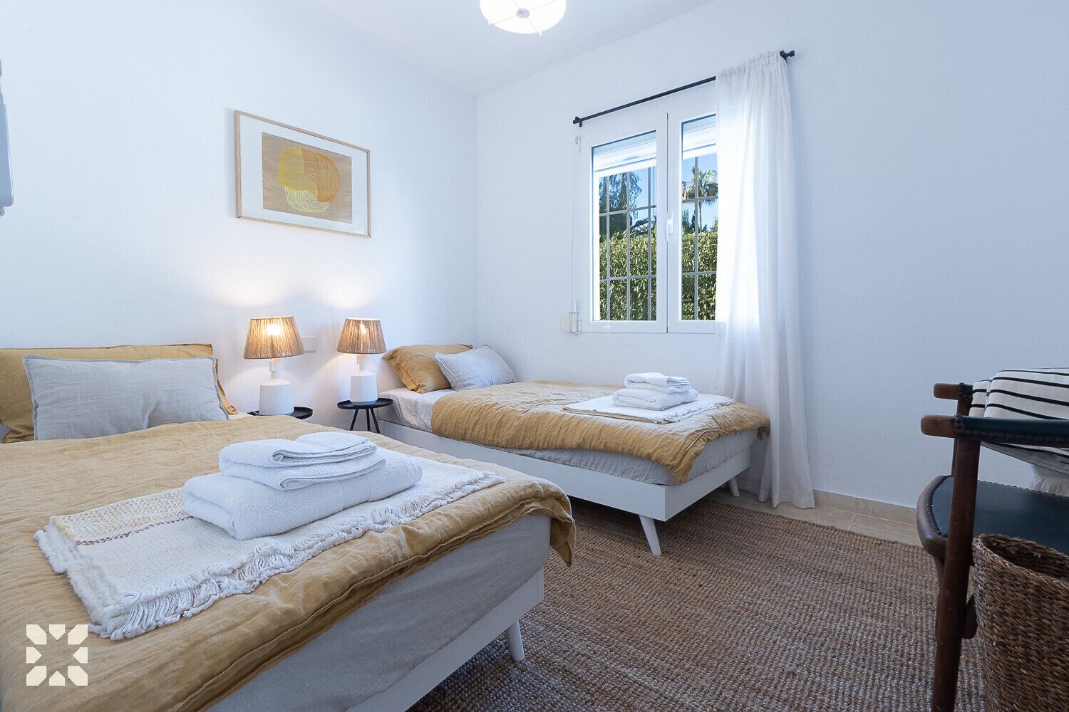 Une chambre d’hôtel avec deux lits, une fenêtre avec des rideaux, une lampe et un tableau encadré au mur.