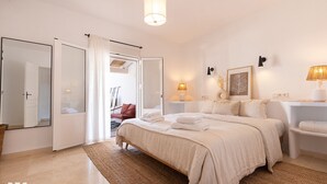 Ein Schlafzimmer mit einem großen Bett, einer Sitzecke mit einem Sessel und Blick auf einen Balkon.