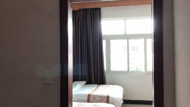 A room with two beds, a window with curtains, and a view of buildings outside. - Mengshan Hotel (Liancheng)