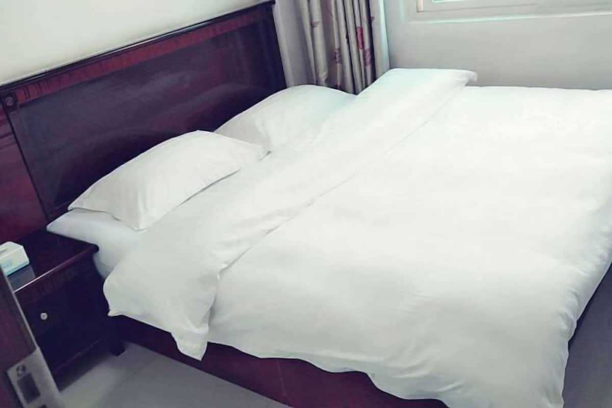 A neatly made bed with white bedding and a wooden headboard.