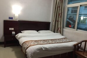 A neatly made bed with white linens and a decorative headboard, a wooden nightstand with a lamp, and a window with curtains. - Mengshan Hotel (Liancheng)