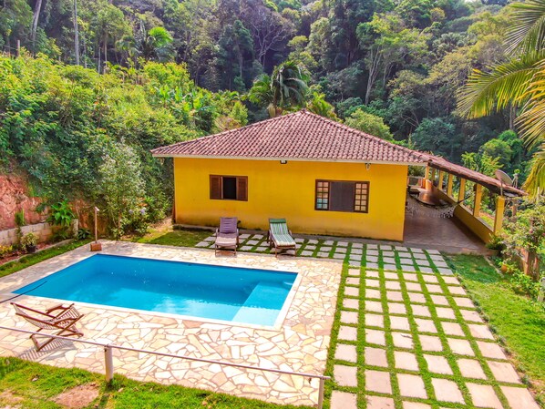 A yellow house with a tiled roof, a swimming pool, and a garden with a stone pathway.