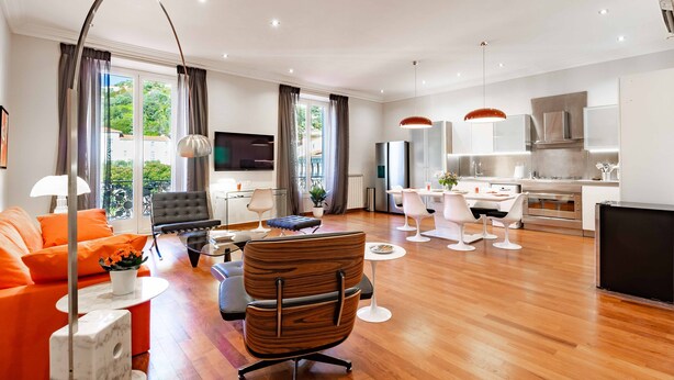 A modern living room with a sofa, a dining area with a table and chairs, a kitchen with a stove, and a TV. - Market Square - 2 bedrooms - 2 baths - private garage - large 90 sq meters (Beaulieu-sur-Mer)