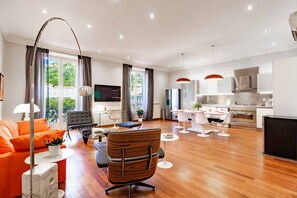 Een moderne woonkamer met een bank, een eethoek met een tafel en stoelen, een keuken met een fornuis, en een televisie.