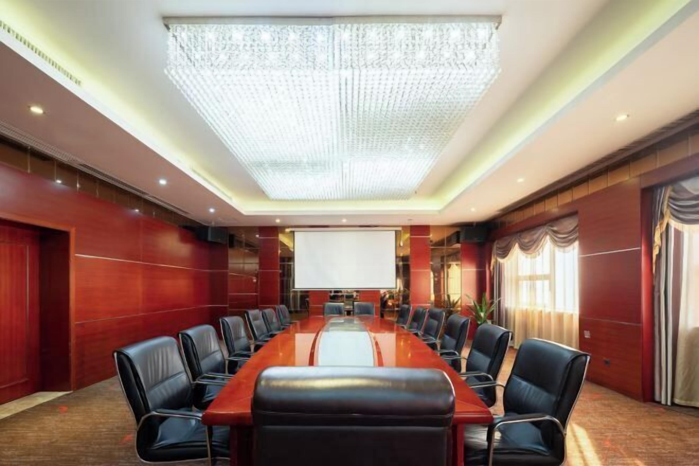 A conference room with a long table, black leather chairs, a large screen, and a chandelier.