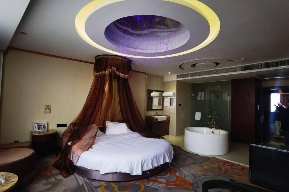 Una cama redonda con dosel, una bañera y zona de ducha en una habitación de hotel moderna.