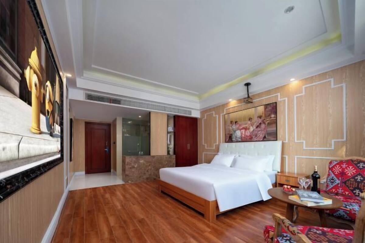 Una habitación de hotel con piso de madera, una cama, un sofá, una mesita y un cuadro en la pared.