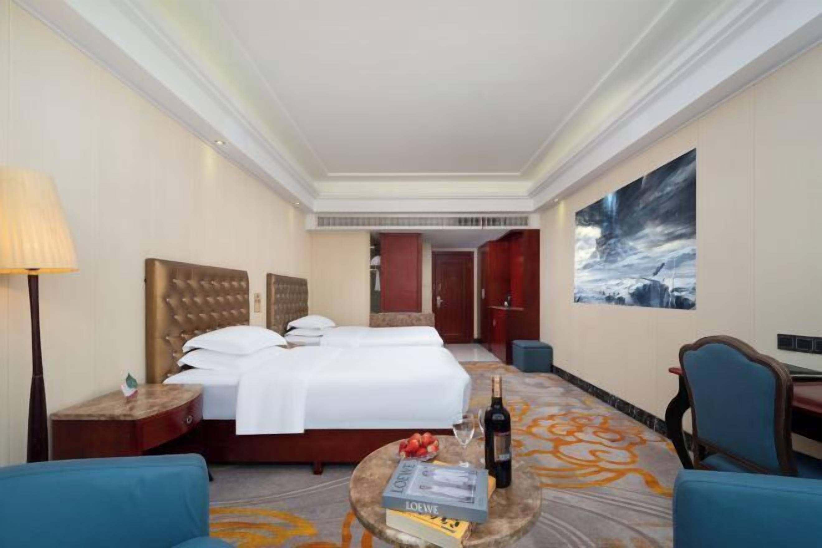 A hotel room with a large bed, a desk, a chair, a lamp, and a painting on the wall.