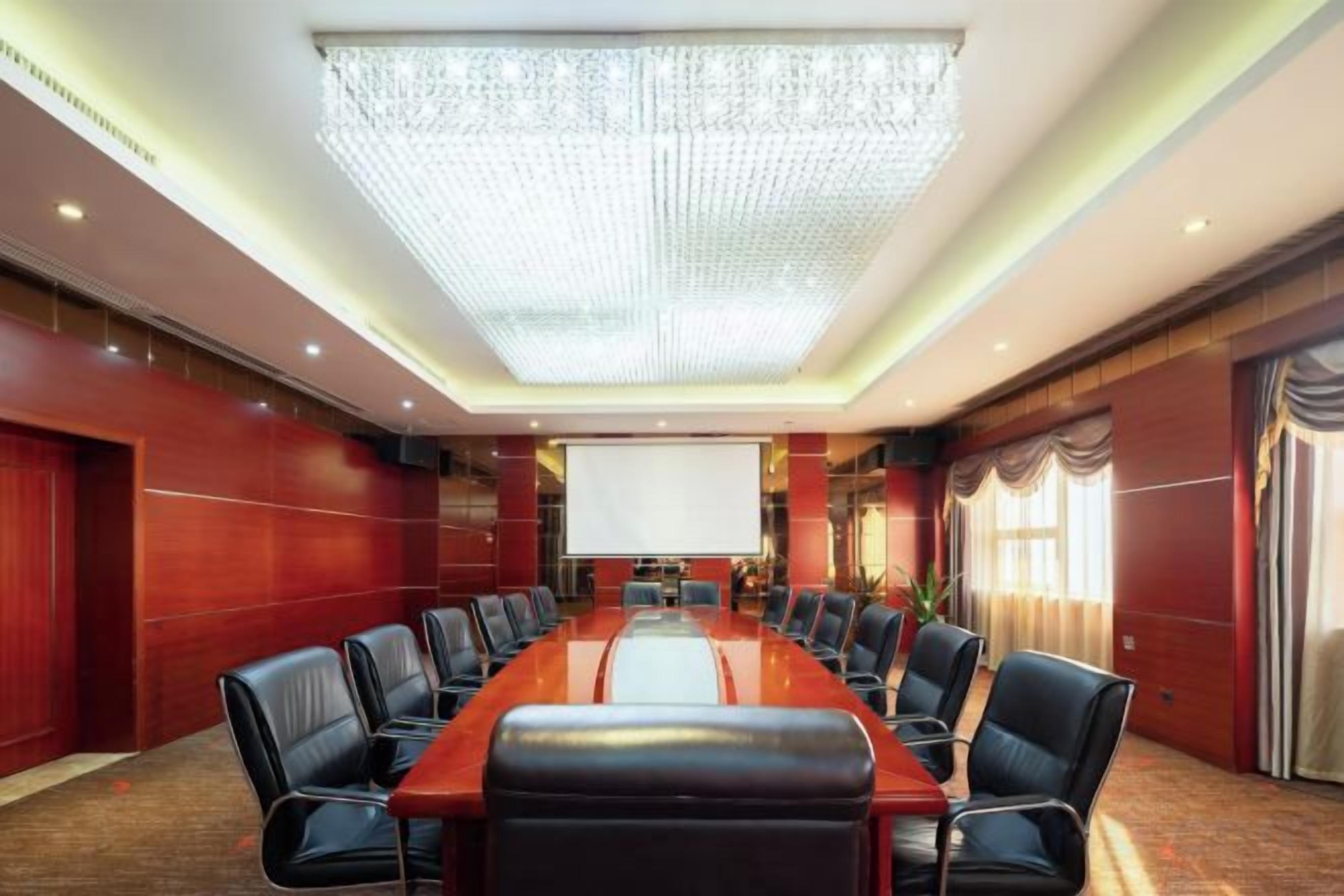 A conference room with a long table, chairs, a projector screen, and a large chandelier.
