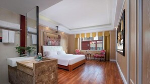 Une chambre d’hôtel avec un grand lit, un coin salon comprenant une chaise et une table, une salle de bain avec un lavabo et un miroir, et une vue sur les bâtiments à travers la fenêtre.