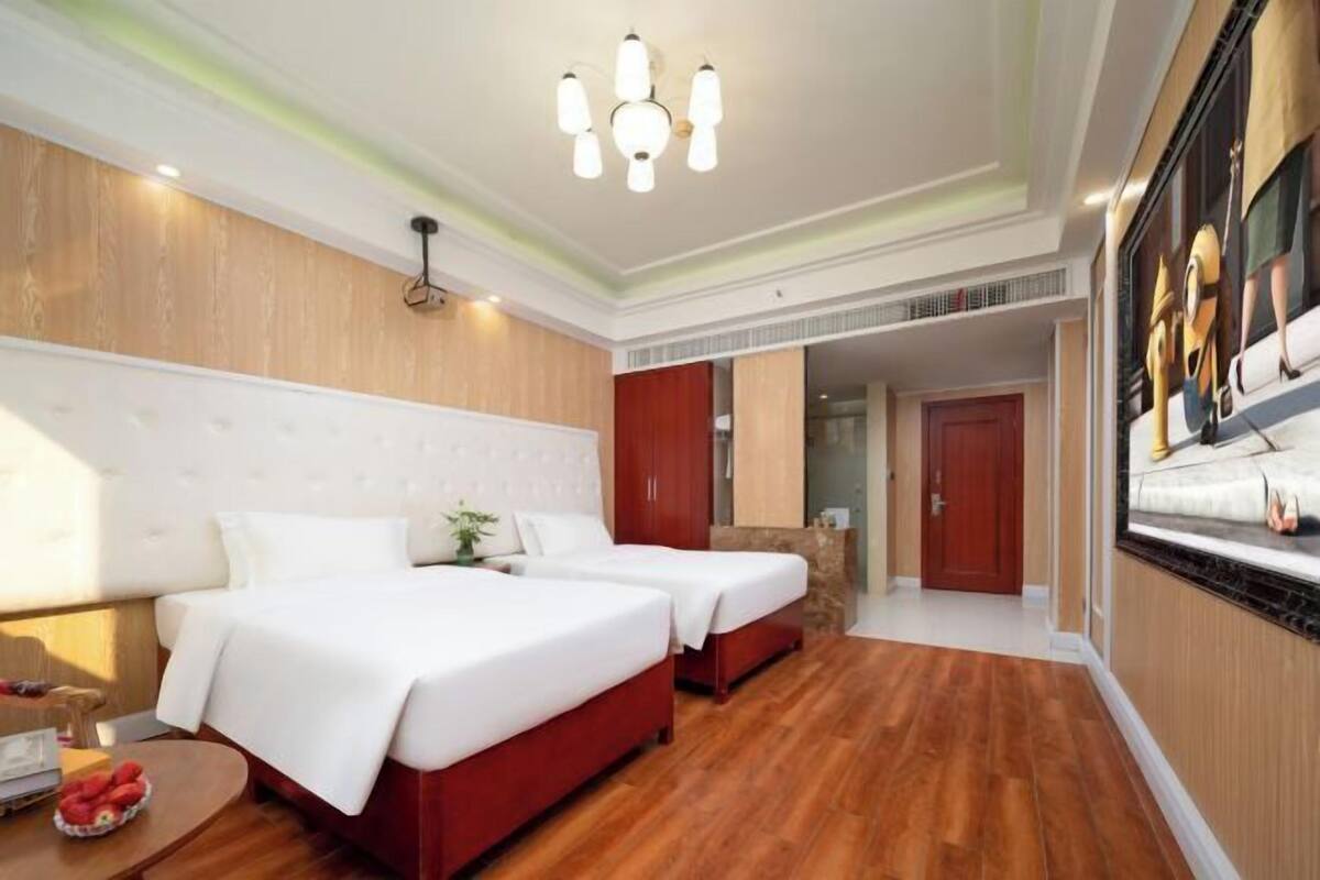 Una habitación de hotel con dos camas, suelo de madera, araña y un espejo grande.