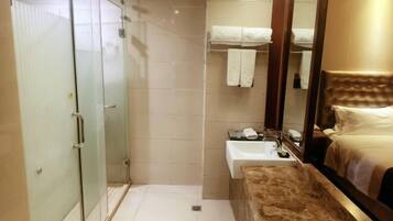 Une chambre d’hôtel dotée d’une douche en verre, d’une tête de lit en bois, d’un lavabo blanc et d’un lit avec une tête de lit.