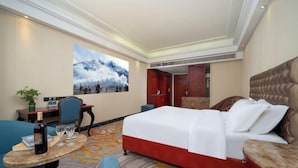 Une chambre d’hôtel avec un lit, un bureau et une chaise, une petite table avec une bouteille et des verres, et un tableau accroché au mur.