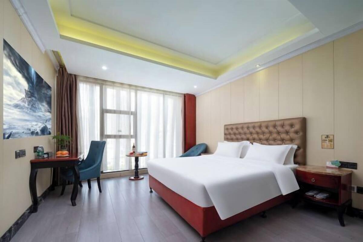 Habitación de hotel con una cama grande, un escritorio, una silla, una mesita y una ventana con cortinas.