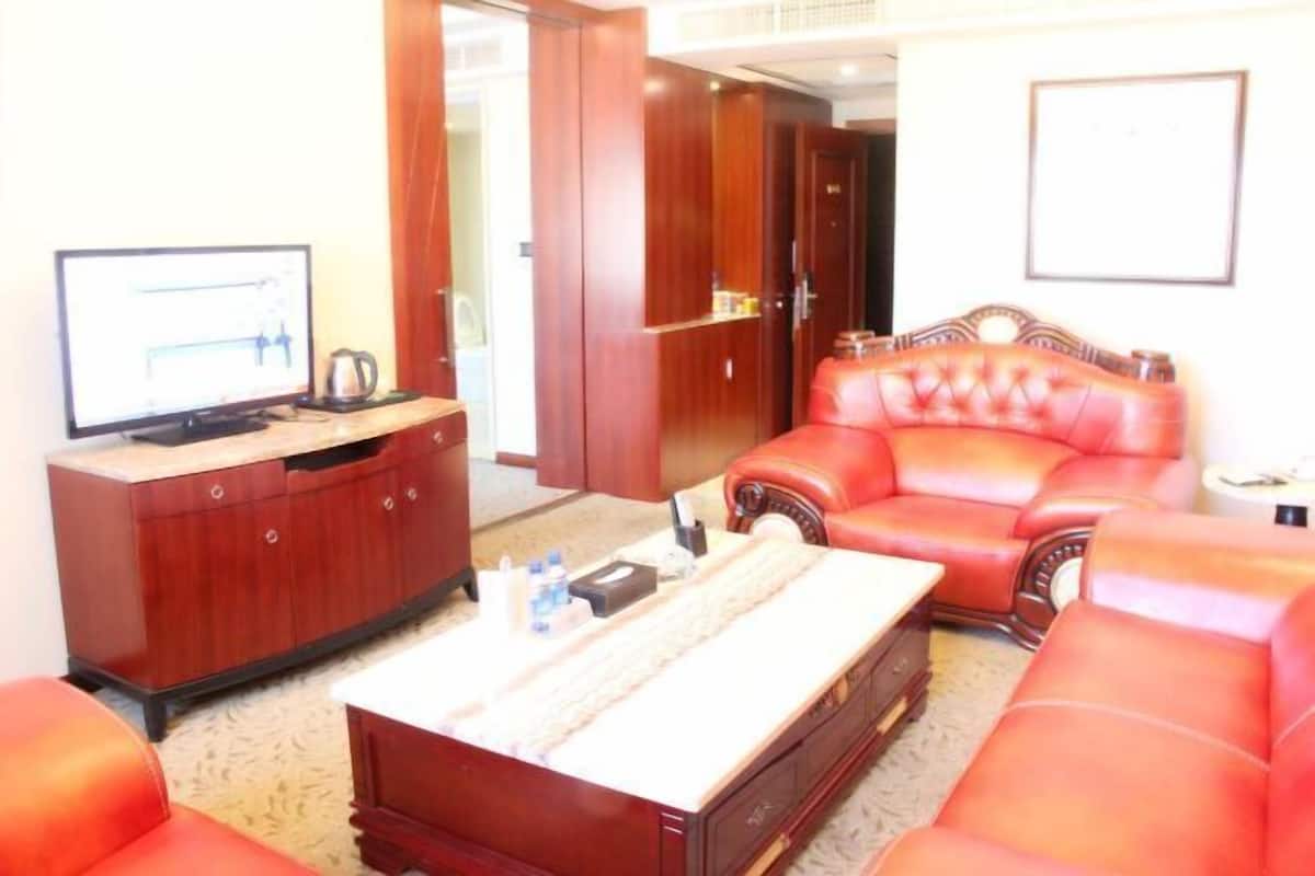 Una sala de estar con un sofá de cuero rojo, una mesa de centro de madera, un televisor y un armario.