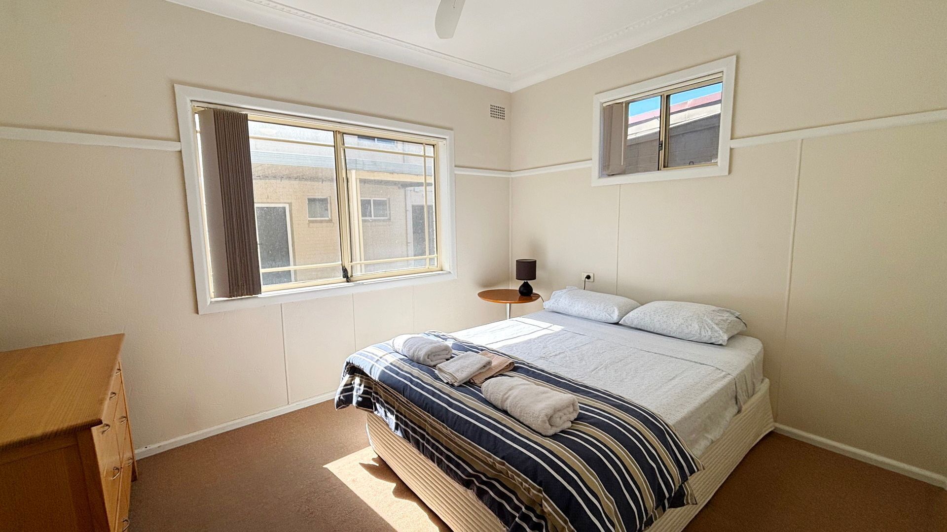 Ein Schlafzimmer mit Bett, Fenster, Nachttisch und Lampe.