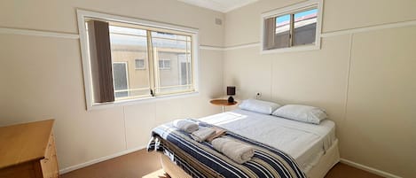 Een slaapkamer met een bed, een raam, een nachtkastje en een lamp.