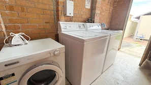 A laundry area with a front-loading washer and dryer, a power outlet, and a brick wall. - Clarkes Flat 1 - town centre unit (SOUTH WEST ROCKS)