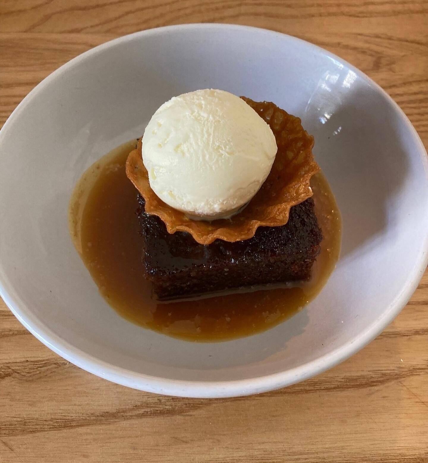 A dessert with a scoop of ice cream on top of a caramelized fruit dish in a white bowl.