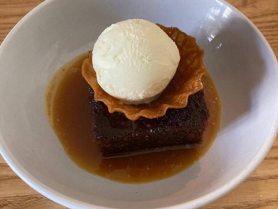 A dessert with a scoop of ice cream on top of a caramelized fruit dish in a white bowl.
