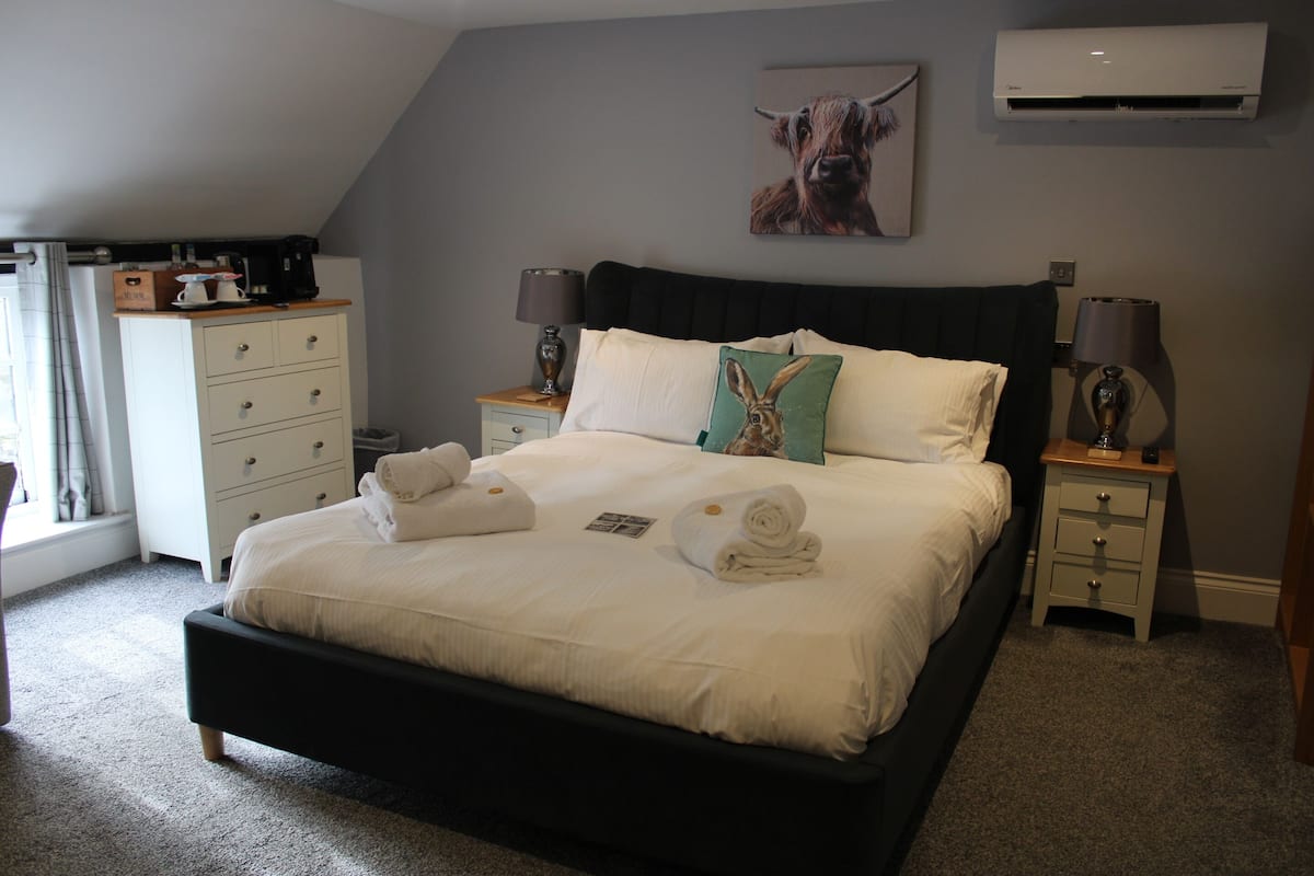 Un dormitorio con una cama grande, dos mesitas de noche, un aparador y un equipo de aire acondicionado en la pared.