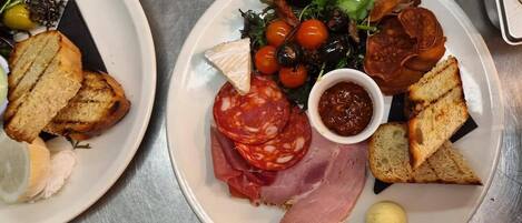 Two plates of food with various items including bread, cheese, salami, olives, and a salad.