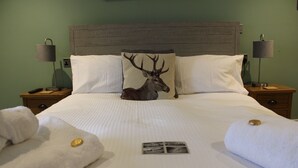 A neatly made bed with a deer pillow, two bedside lamps, and a small photo frame on the bed. - The White Lion (Ventnor)