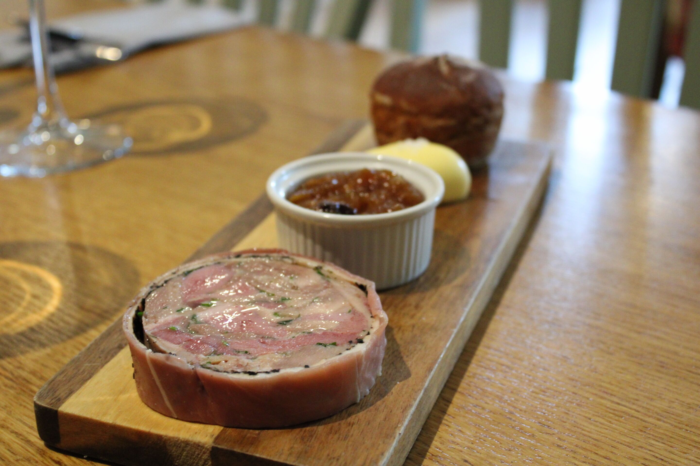 A wooden table with a meat dish, a small bowl of sauce, and a pastry.