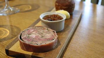A wooden table with a meat dish, a small bowl of sauce, and a pastry.